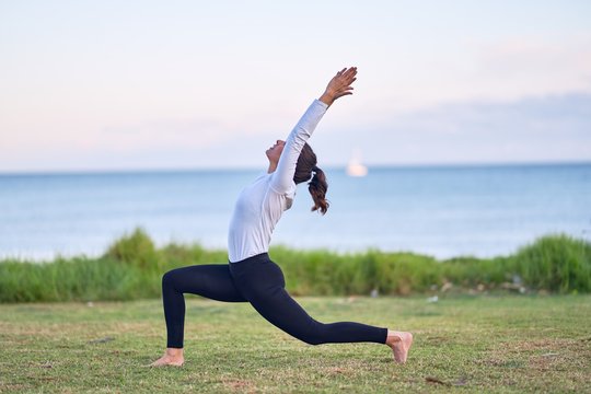 Young beautiful sportwoman practicing yoga. Coach teaching warrior pose at park