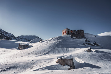 Ice and snow covered small stone  shelter hut standing on top of the peak at winter