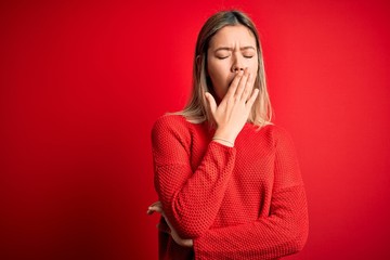 Young beautiful blonde woman wearing casual sweater over red isolated background bored yawning tired covering mouth with hand. Restless and sleepiness.