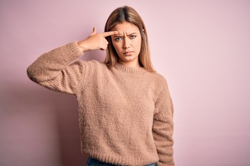 Young beautiful blonde woman wearing winter wool sweater over pink isolated background pointing unhappy to pimple on forehead, ugly infection of blackhead. Acne and skin problem