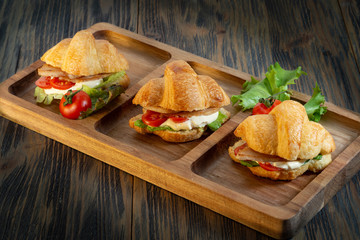 Croissants with cream, tomatoes and herbs on wooden background
