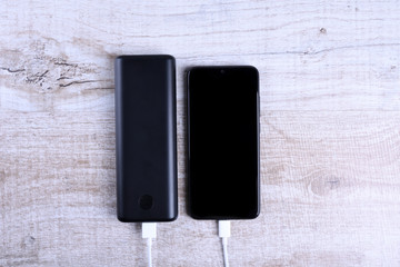Phone charging,powerbank charges smartphone,cellphone with energy bank. Depth of field on Power bank on wooden background