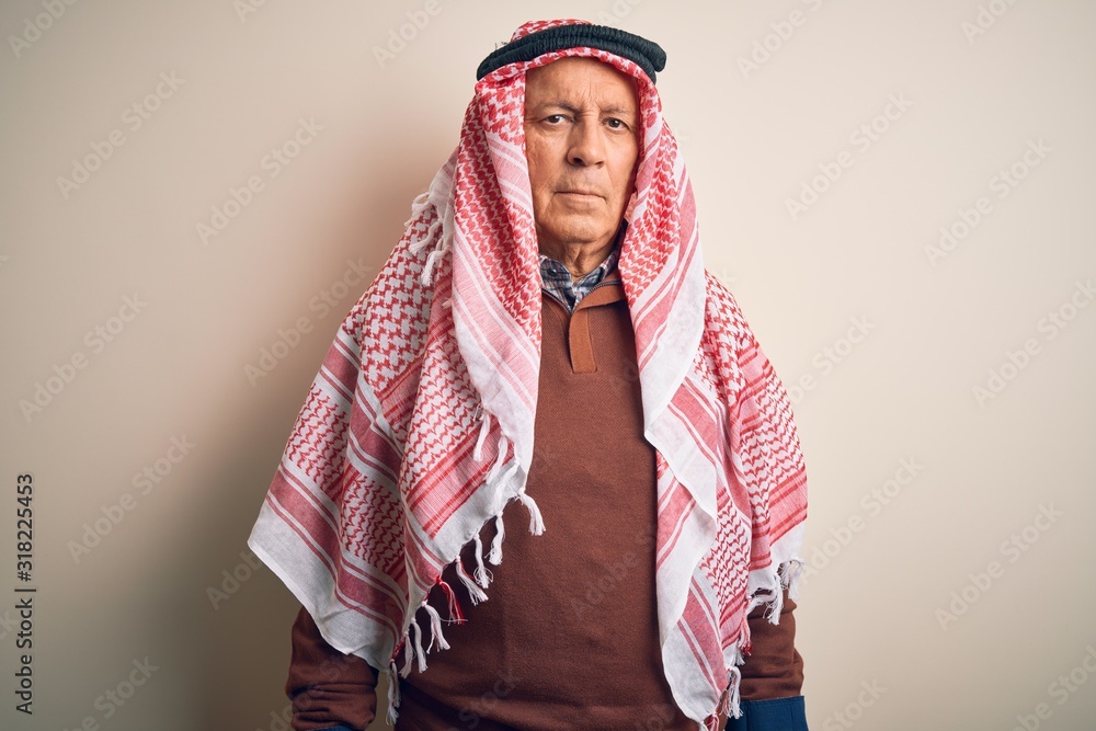 Wall mural senior handsome arab man wearing keffiyeh standing over isolated white background with serious expre