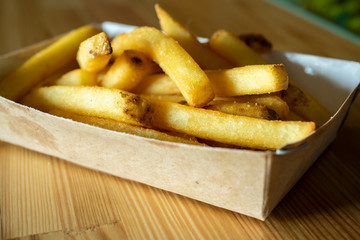 French fries in a paper container on a table made of light wood.