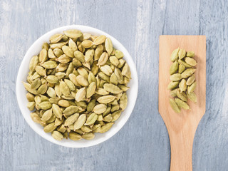 Spice green cardamom (Elettaria cardamomum) in a ceramic white bowl and wooden spatula. Modern apothecary, naturopathy and ayurveda concept