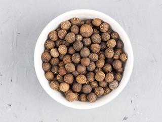 Allspice in a white bowl on a gray concrete background. Healthy eating concept