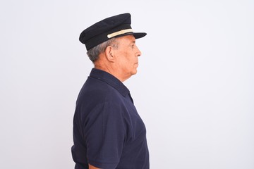 Senior grey-haired man wearing black polo and captain hat over isolated white background looking to side, relax profile pose with natural face with confident smile.