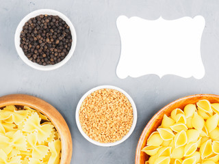 Different types of pasta in wooden bowls, fenugreek, black pepper on a gray concrete background with copy space. Healthy eating concept