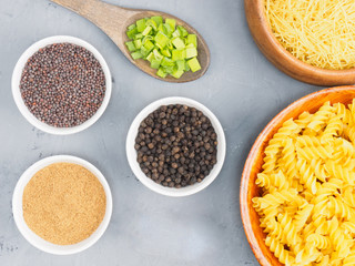 Pasta in wooden bowl, mustard seed, masala, black pepper, green onion on a gray concrete background. Healthy eating concept