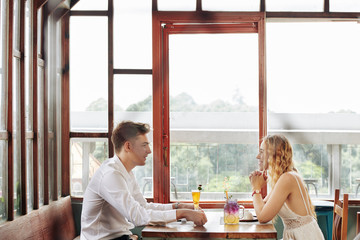 Horizontal through window side view shot of young man and woman spending time together in romantic restaurant