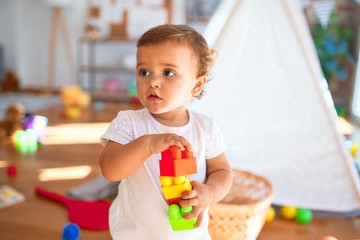 Adorable toddler playing with building blocks around lots of toys at kindergarten