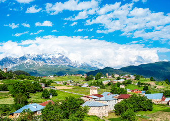 Fototapeta premium Village houses with towers on the background of Tetnuldi Mountain. Svaneti mountain landscape on sunny summer day . Caucasus Mountains, Georgia