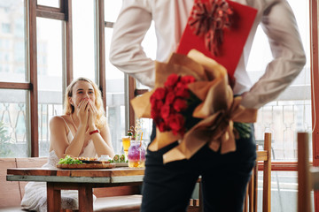 Horizontal shot of unrecognizable young man showing up for date in cafe with rose bouquet and box...