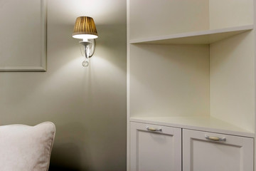 Sconce on the wall near the sofa and cabinet with shelves. Electric lighting