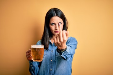 Young woman with blue eyes drinking jar of beer standing over isolated yellow background Showing...