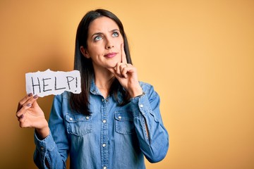Young brunette woman with blue eyes holding for help and protection with help word text serious face thinking about question, very confused idea