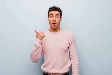 young arabian man looking astonished in disbelief, pointing at object on the side and saying wow,...