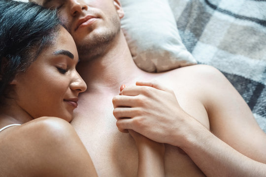 Mixed Race Couple. Young man and woman lying on bed on blanket top view sleeping holding hands smiling peaceful close-up