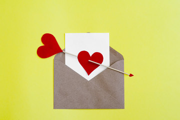 White card in craft envelope with red paper hearts and Cupid's arrow on yellow background