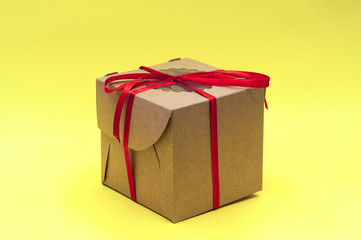 brown craft gift box with red ribbon bow on yellow background