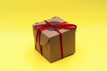 brown craft gift box with red ribbon bow on yellow background