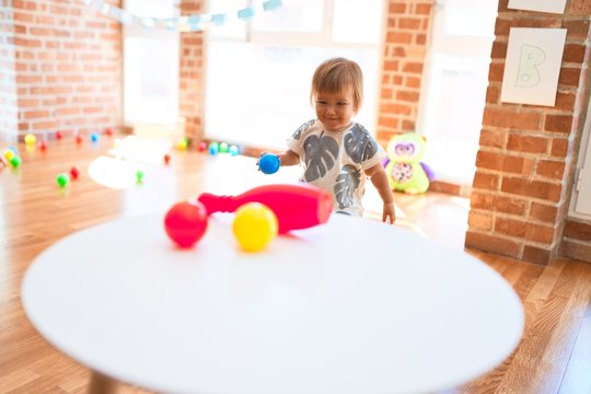 Adorable toddler playing with balls around lots of toys at kindergarten