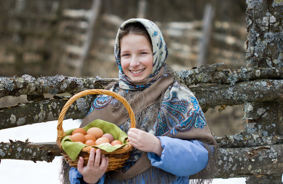 A young girl in a Russian scarf with a basket of chicken eggs. The concept of a Russian village and Easter.