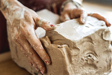 Craftsperson Concept. Young woman making pottery indoors modeling clay hands close-up