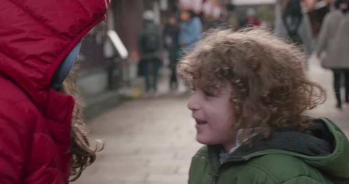 Young girl in a red parka playfully squeezes the cheeks of a young boy as they pose for photos on a historic street in Kanazawa Japan