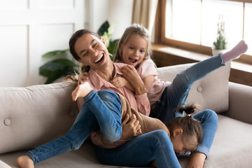 Overjoyed young mom and daughters have fun at home