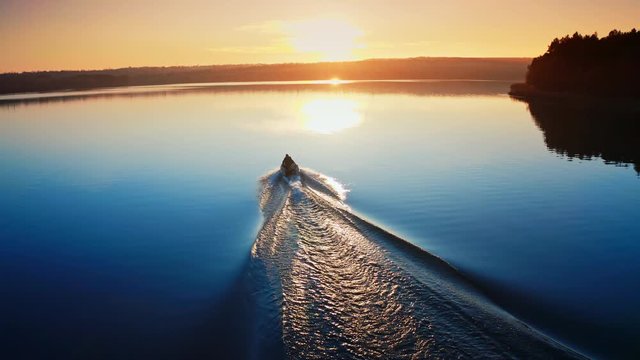 Motor boat floating on the river at sunset. Path on water after motion of motor boat on the background of a setting sun.