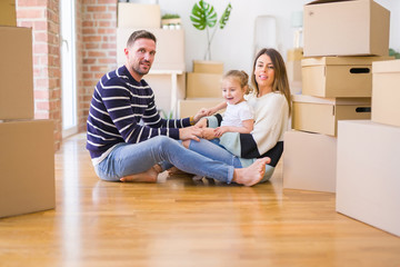 Beautiful family sitting on the floor playing with his kid at new home around cardboard boxes