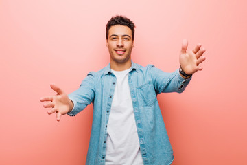 young arabian man smiling cheerfully giving a warm, friendly, loving welcome hug, feeling happy and adorable against pink wall