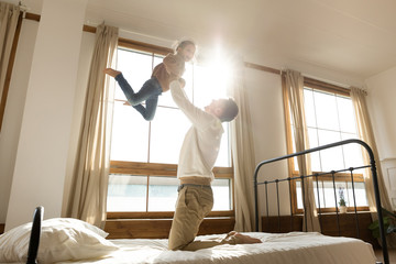 Overjoyed dad and little daughter play in bedroom