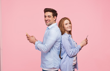 Modern couple using phones and smiling at camera