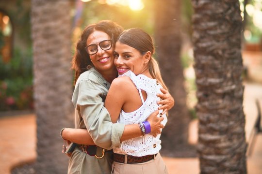 Beautiful mother and daughter smiling happy and confident. Standing with smile on face hugging at town park