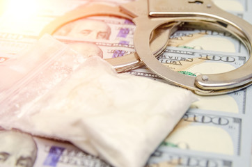 Handcuffs and a bag of drugs close up on dollar bills