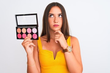 Young beautiful girl holding makeup standing over isolated white background serious face thinking about question, very confused idea