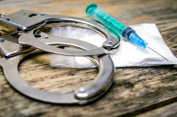 Handcuffs, syringe, bag of drugs on a wooden background close-up