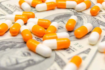 A lot of white and orange tablets on the background of dollar bills close-up. Concept of insurance, medicine, macro
