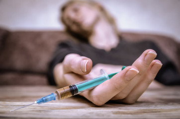 young girl with a syringe in her hand is sitting on the sofa, with a syringe in focus. The concept of overdose