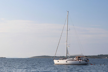 Obraz premium A modern sailing yacht is anchored in a bay. People bathe in the sea. Active rest on the Adriatic Sea of the Mediterranean region. Dalmatian riviera of Croatia. Prestigious and rich lifestyle