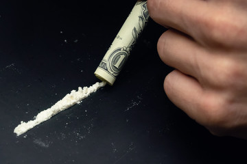 Male hands sniffing drugs through a dollar on a black background close up