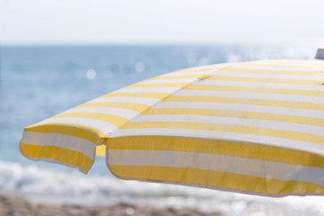 umbrella with yellow stripes over a deck chair on the beach, against the sea with sun glare