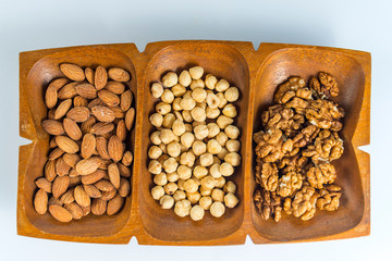Flat laid healthy raw snack of nuts served in a wooden container, shot from above and isolated on white background. Raw almonds, raw hazelnuts, raw walnuts.