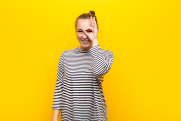 young blonde pretty girl smiling happily with funny face, joking and looking through peephole,...