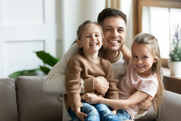 Fototapeta premium Happy dad cuddle little daughters relaxing together at home