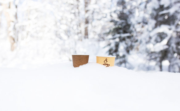 Two paper cups for a drink stand in a snowdrift in the winter. The theme of ecology and garbage collection.