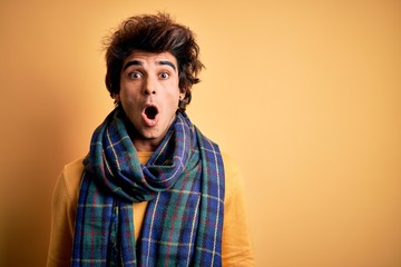 Young handsome man wearing casual scarf standing over isolated yellow background afraid and shocked...