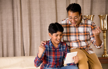 Father and son astonished on receiving good news using digital tablet
